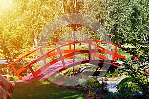 wooden red decorative bridge across the pond, sunlight effect