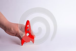 Wooden red rocket in hand on a white background. A man is playing with a rocket. Minimalism, space travel and tourism