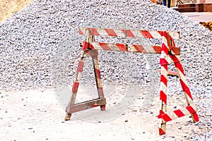 Wooden red-white fencing roadblock and heap of rubble on a road construction at city street