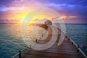 Wooden road from the island to a hut over water on a sunset. Maldives