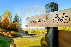 A wooden road sign showing a direction for a mountainbike path. A sunny autumn day for a bike tour through the nature.