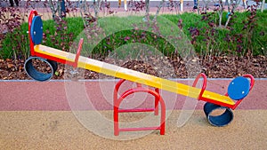 A wooden rocking chair of yellow red color with chairs on the playground with a rubberized coating