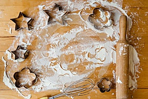 A wooden rolling pin and metal shaped cookie cutters on a floured table