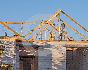 Wooden roof frame of residential building under construction. Unfinished house of white brick with holes for windows
