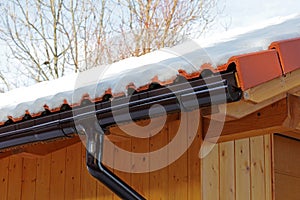 Wooden roof with rain gutter and drainpipe in winter