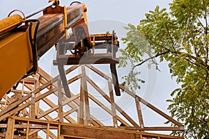 A wooden roof truss being lifted by a boom truck forklift in the roof a new home