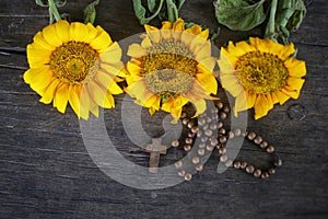 Wooden Rosary with Jesus Christ Cross Crucifix and three beautiful sunflwoers blossom arrangement on rustic table background.