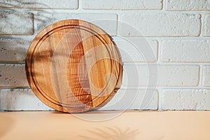 Wooden round board on orange table with shadow from palm tree with free space for inscription in a white brick wall