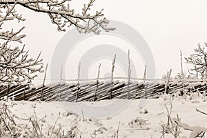 A wooden roundpole fence in winter, covered in snow.