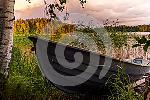 A wooden rowing boat at Sunset on the shores of the calm Saimaa lake in Finland under a nordic sky with a rainbow - 1