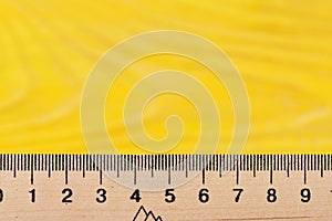 Wooden ruler close up on yellow background.
