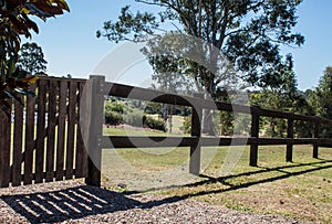 Wooden rural fence and gate in sunshine with trees in background