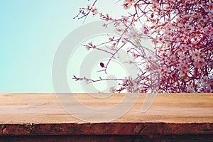 wooden rustic table in front of spring cherry blossoms tree. vintage filtered image. product display and picnic concept.