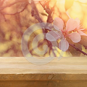 wooden rustic table in front of spring cherry blossoms tree. vintage filtered image. product display and picnic concept.