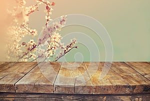 Wooden rustic table in front of spring white cherry blossoms tree. vintage filtered image. product display and picnic concept