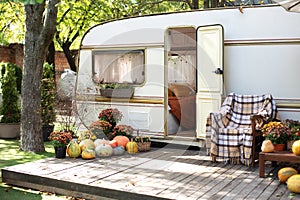 Wooden RV house porch with garden furniture. Interior cozy yard campsite with fall flowers potted and pumpkins.