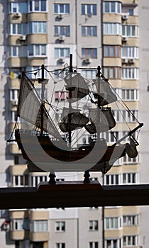 Wooden sailboat model on a wooden railing with blurred multi storey house building on a background