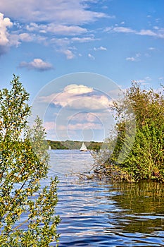 Wooden sailing boat between trees on Lake Schwerin with clouds