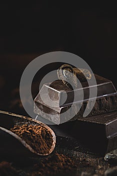 Wooden scoop with cocoa powder and piece of block chocolate with cacao beans