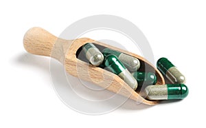 Wooden scoop with green spirulina capsules on white