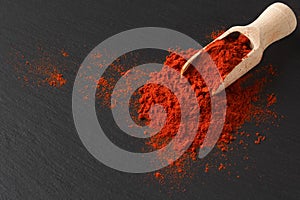 Wooden scoop with ground paprika on black textured background, close up