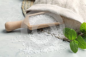 Wooden scoop with natural sea salt, sack and mint on light grey marble table, closeup