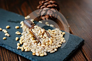 wooden scoop with pine nuts inside it over the stone slate.