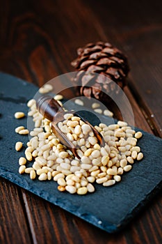 wooden scoop with pine nuts inside it over the stone slate.