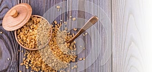 Wooden scoop spoon and bowl full of brown cane sugar with pinch of sugar spilled around on wooden table, top view