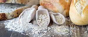 Wooden scoops of wheat flour, oats and oat bran with bread and buns in behind.