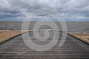 A wooden seside slipway leading across a peeble beach