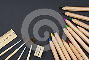 Wooden set of colored pencils, sharpener, brushes and ruler on black background