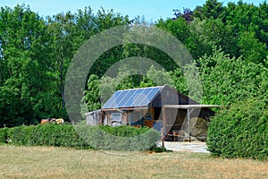 Wooden shack with solarpanels in a field with green trees background