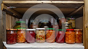 Wooden shelf in pantry with provisions in glass jars with pickled vegetables photo
