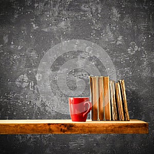 Wooden shelf with red mug, books, empty copy space for your decoration and products and gray retro wall background. Home interior.