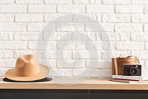 Wooden shelf with retro photo camera and hat. Stylish interior of living room with white brick wall, brown box, elegant accessorie