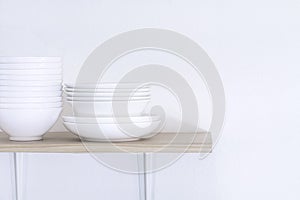 Wooden shelf template isolated on white wall background which on set stacked white bowls and plates as items tableware for