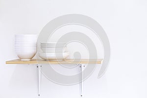 Wooden shelf template isolated on white wall background which on set stacked white bowls and plates as items tableware for