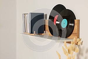 Wooden shelf with vinyl records and books on white wall