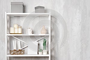 Wooden shelving unit with decor near grey wall. Bookcase with photo frame mockup and candles, living room interior details