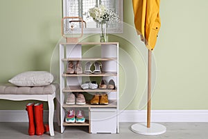 Wooden shelving unit with shoes and different accessories near green wall in hall. Storage idea