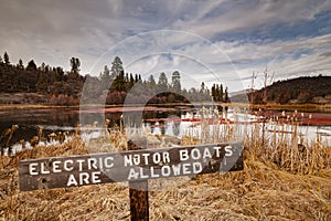 Wooden sign at Baum Lake  advising people that electric powered vessels are permitted.  Shot in mid winter with moody clouds