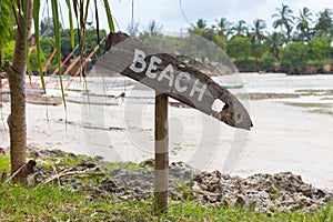 Wooden sign Beach on tropical coast. Low tide landscape with signpost Beach. Beach with palm trees and boats. Paradise direction.