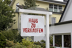 Wooden sign in front of a house with message For Rent, For Sale, and the german words for sale - zu verkaufen photo