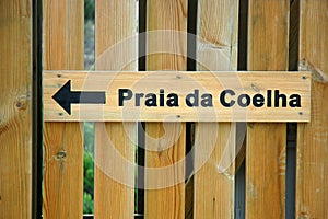 Wooden sign installed on a wooden fence showing direction towards Praia da Coelha or Rabbit Beach, Algarve, Portugal