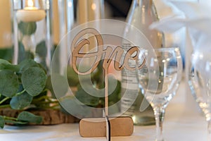 Wooden sign with the number "one" prominently displayed standing near a glasses and candles