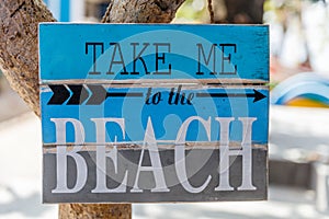 Wooden sign TAKE ME TO THE BEACH with an arrow on a tree at Pantai Sanur, Bali, Indonesia