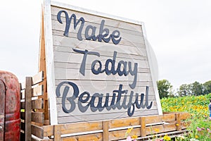 Wooden sign on tractor that says Make Today Beautiful in cursive writing in a flower field