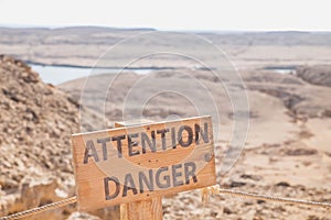 wooden sign with the word "attention, danger" on top of a cliff in the desert in Egypt