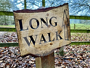 Wooden Sign with wording Long Walk. Wooden fence behind with grass and trees.